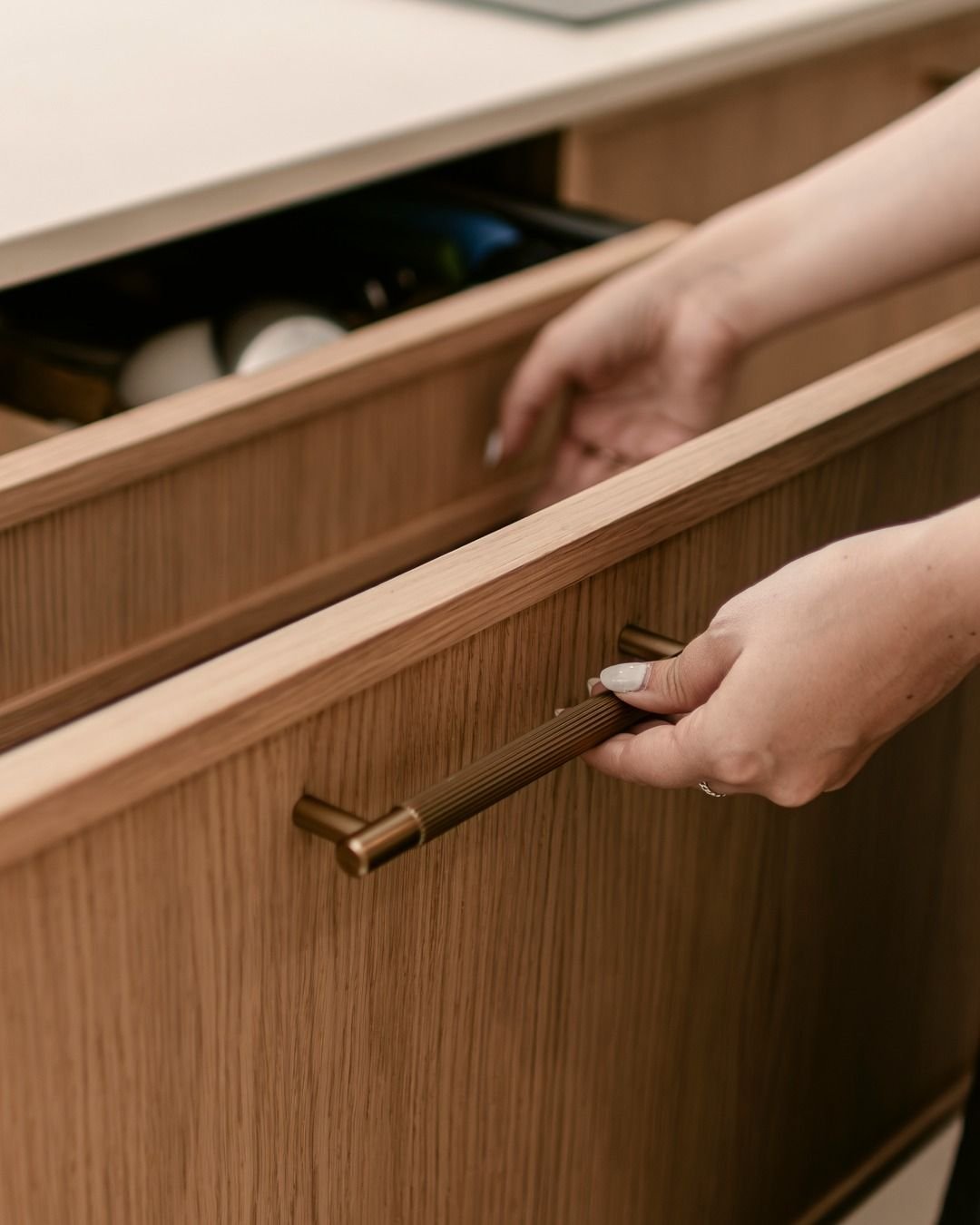 A hand opening a fluted oak drawer by a fluted brass pull, with a soft-close drawer box behind it.