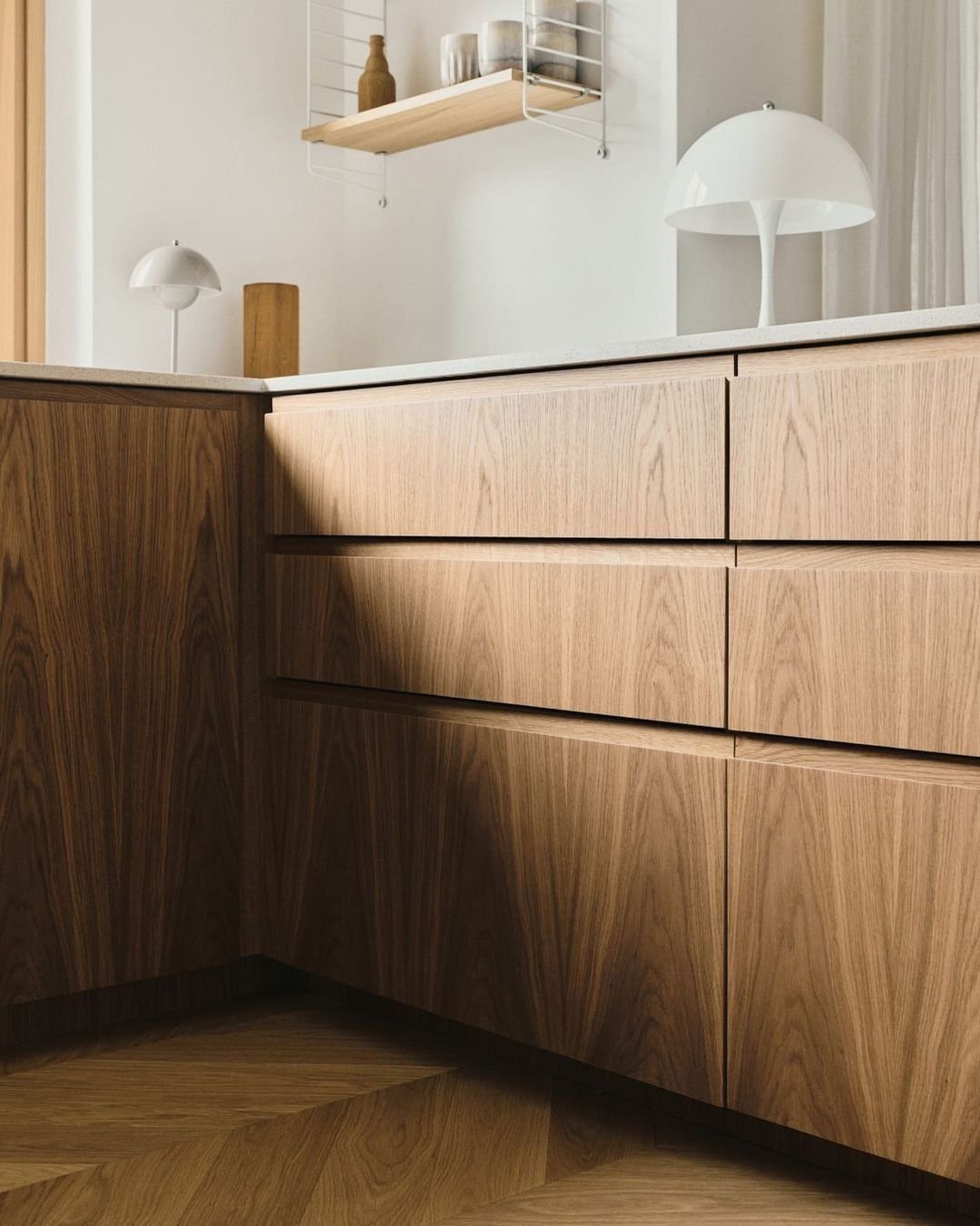Oak kitchen run with handleless grain-matched drawer fronts meeting at a mitered corner under a stone countertop.
