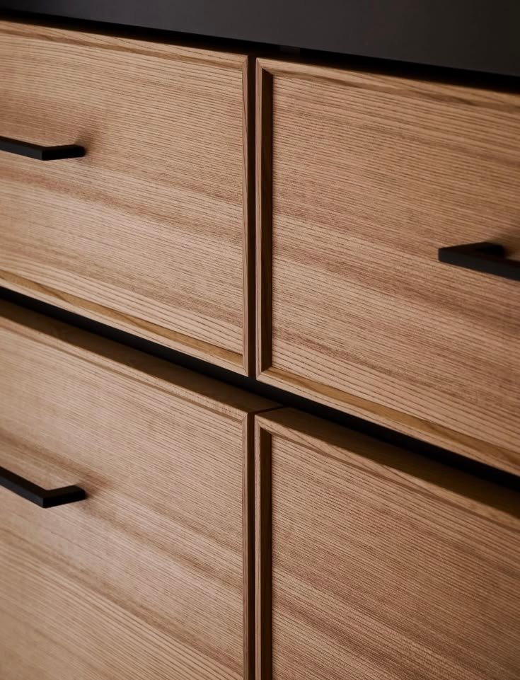 Close-up of ash drawer fronts with mitered edge profiles and matte black bar pulls, showing tight, even reveals.
